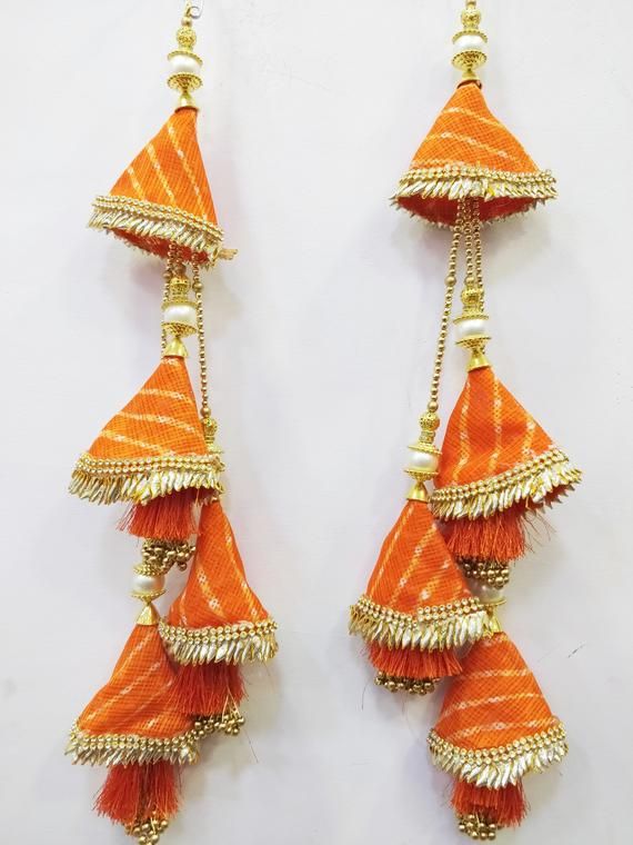 two orange and gold earrings with tassels hanging from the side on a white background