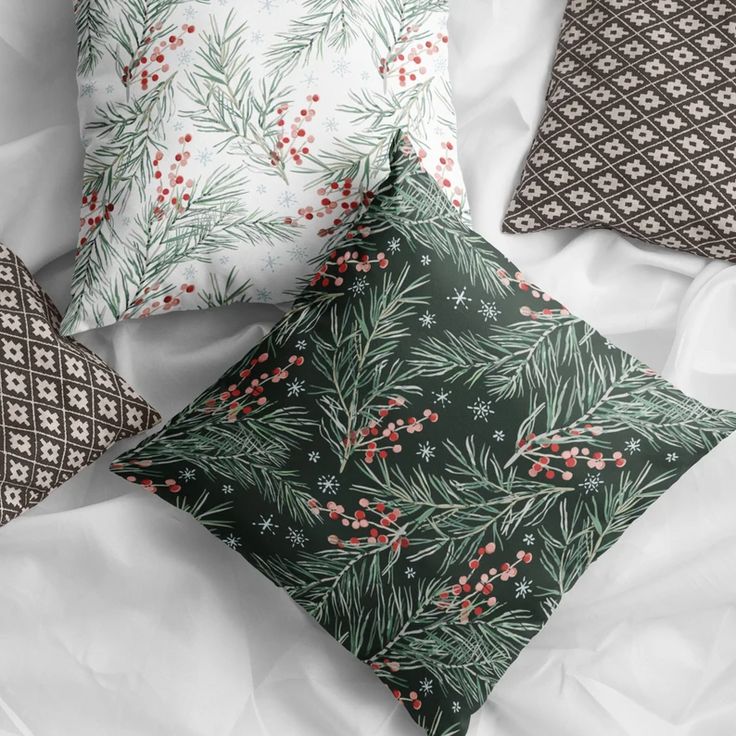 three decorative pillows on a bed with white sheets and black and green patterns, one is decorated with red berries