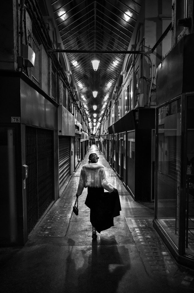 a woman walking down a long hallway holding an umbrella over her head in black and white