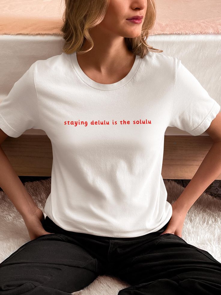 Add a touch of humor to your wardrobe with our "Staying Delulu is the Solulu" Quote T-Shirt! Perfect for those who love a good laugh and believe in staying positive, this tee is a fun way to embrace a lighthearted approach to life. Whether you're out with friends, at a casual gathering, or simply enjoying a relaxed day, this shirt is sure to bring smiles and chuckles. Materials and Quality: Our t-shirt is made from premium, soft cotton that feels gentle against your skin, making it ideal for everyday wear. The high-quality print ensures the quote remains vibrant and clear, even after many washes. Available in a variety of sizes to fit all body types comfortably. Usage and Versatility: This versatile tee is perfect for casual outings, relaxed weekends, or as a humorous gift for friends and Funny Text Stretch Short Sleeve T-shirt, Stretch Cotton T-shirt With Funny Text, Cotton Stretch T-shirt With Funny Text, Stretch Crew Neck T-shirt With Slogan, Staying Delulu, Funny Messages, Good Jokes, Staying Positive, Funny Quote