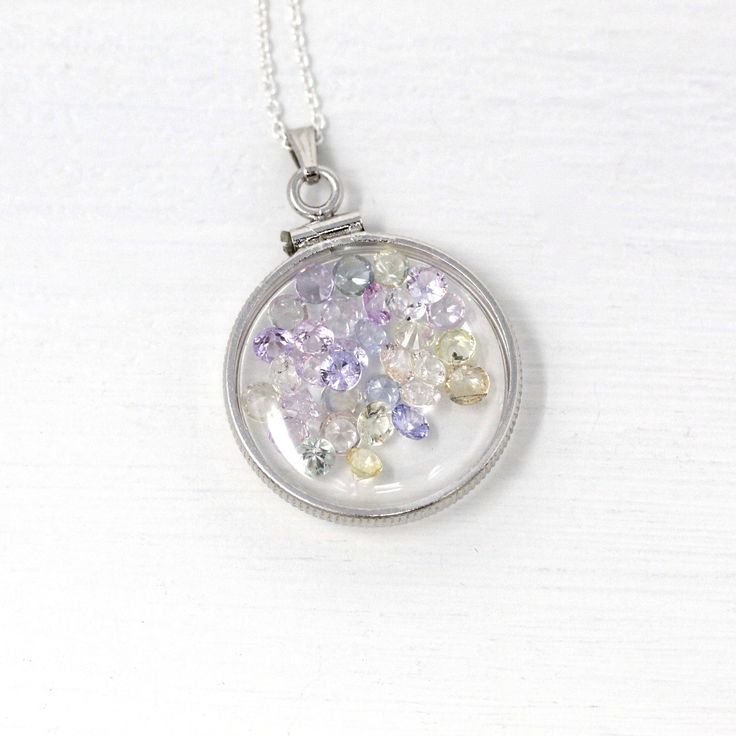 "Magical handcrafted brand new sterling silver genuine sapphire shaker locket! This classic pendant is nickel sized with coin style bezels, and clear lucite covers. The round statement charm hangs from a brand new sterling silver chain, and is filled with 4.5 carats of round faceted genuine pastel colored sapphire gems. A gorgeous piece of gemstone jewelry, featuring pastel multi-colored sapphires! ERA - New METAL / MATERIAL - Sterling silver locket, sterling silver chain, lucite clear covers, 1 Sapphire Round Pendant Jewelry, Silver Sapphire Necklace Hallmarked, Silver Round Locket Jewelry, Sterling Silver Pendant Locket Necklace With Polished Finish, Sterling Silver Locket Necklace With Polished Finish, Handmade Sterling Silver Locket Necklace, Sapphire Round Pendant Jewelry For Gift, Handmade Sapphire Round Necklace, Unique Round Coin Pendant Jewelry