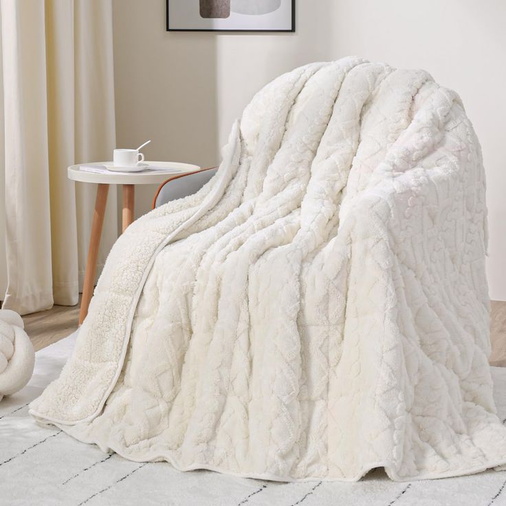 a large white blanket sitting on top of a bed next to a table and chair