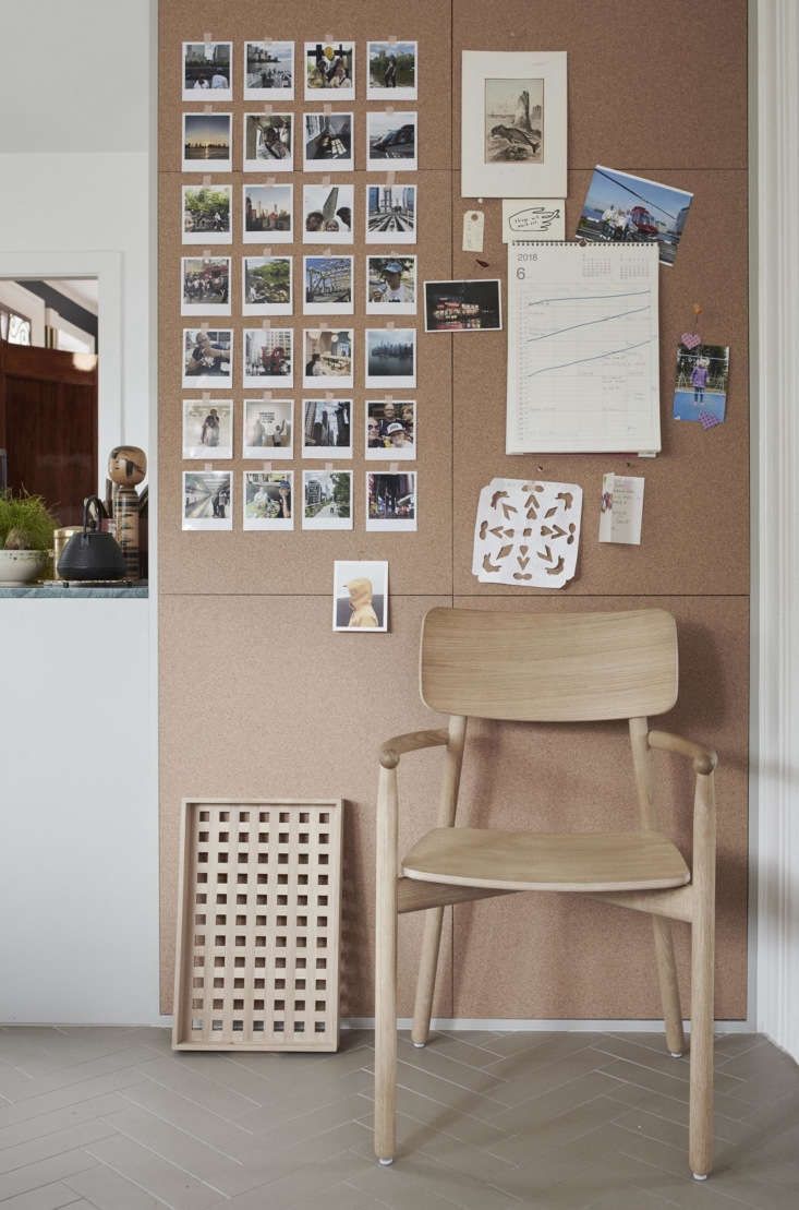 a wooden chair sitting in front of a cork board with pictures on the wall behind it