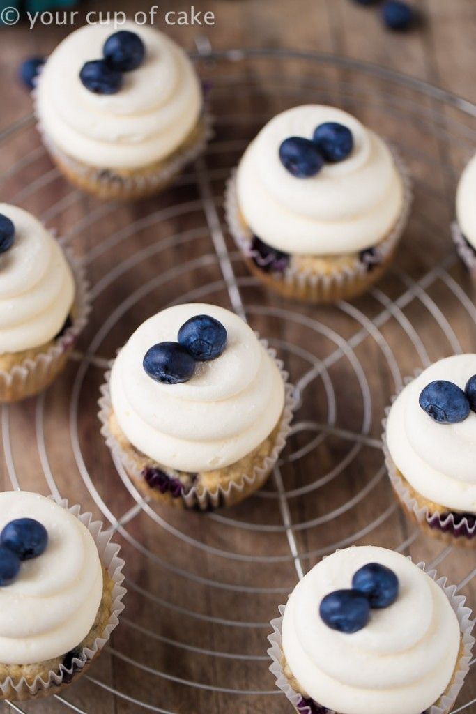 cupcakes with white frosting and blueberries are arranged on a wire rack