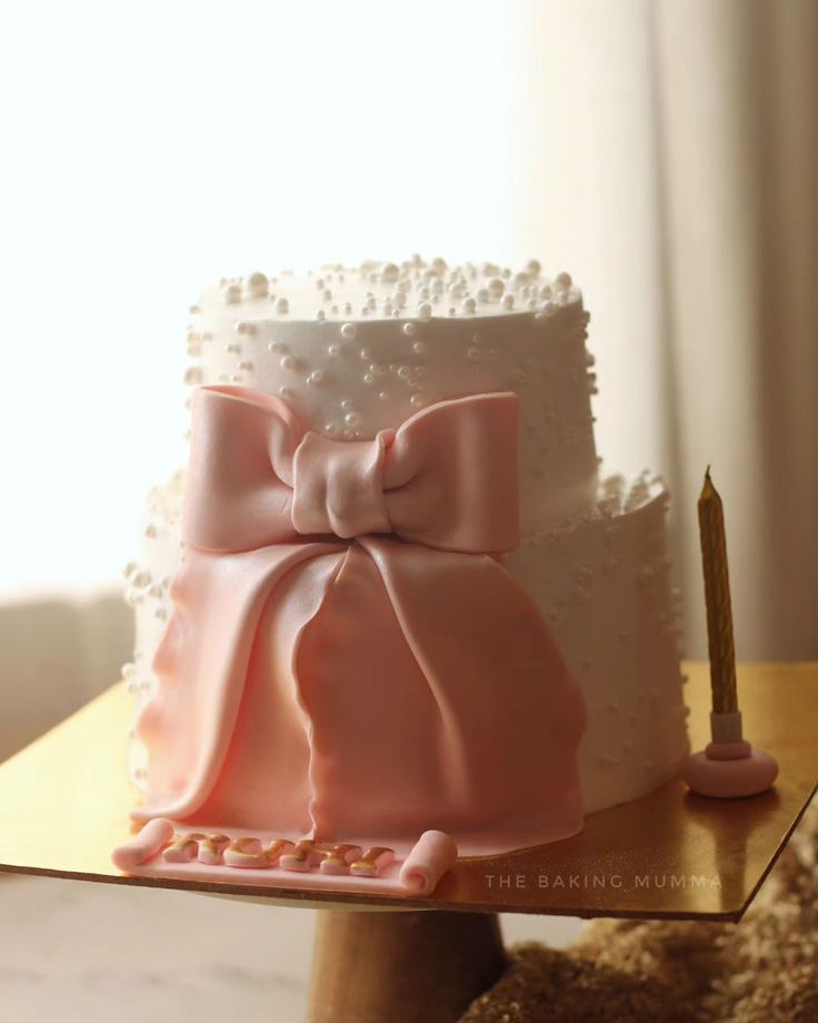 a three tiered cake decorated with pearls and a pink bow