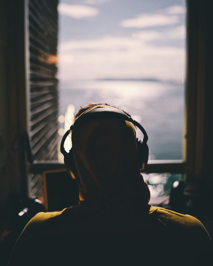 a man wearing headphones looking out the window at the ocean and city lights in the distance