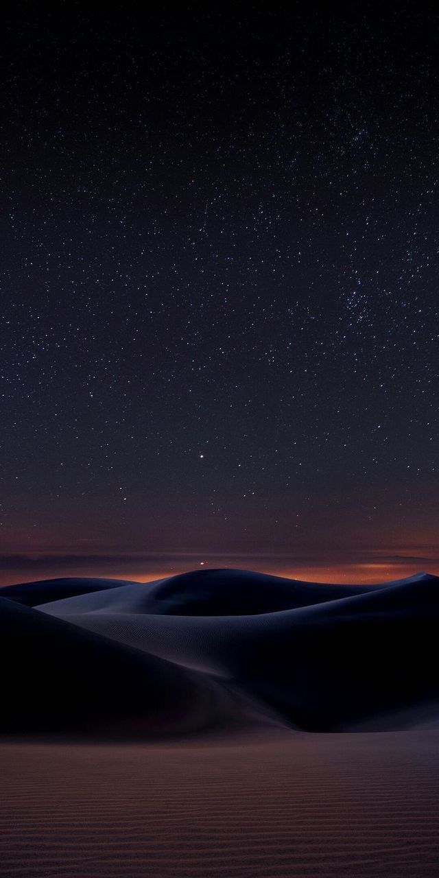 the night sky is lit up over sand dunes and stars in the distance, as seen from