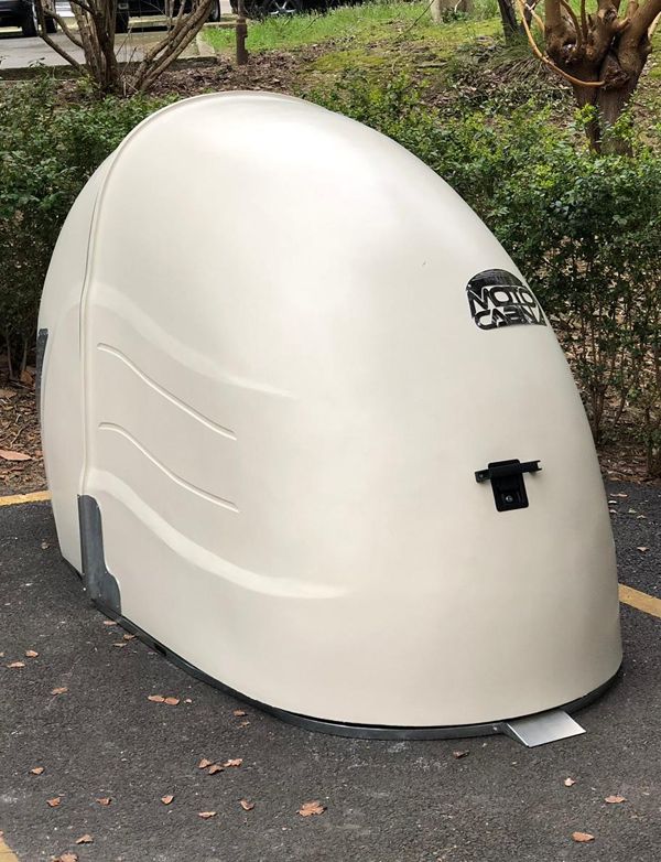 a large white object sitting in the middle of a parking lot next to trees and bushes