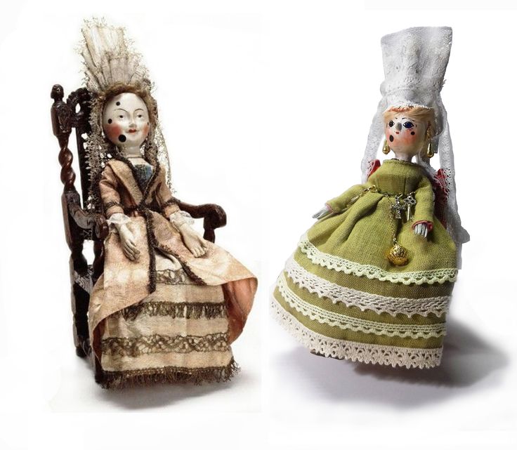 two dolls sitting next to each other on top of a white surface and one is wearing a green dress