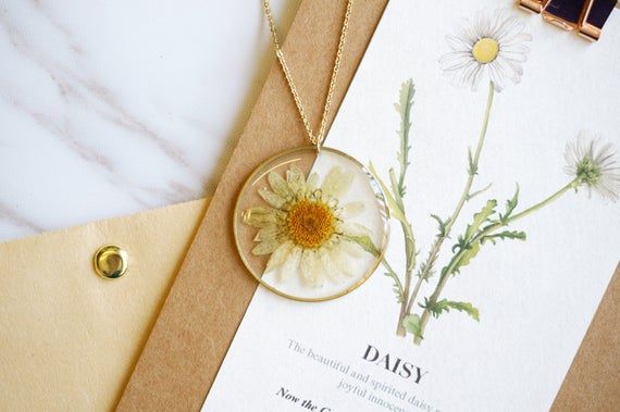 a necklace with daisies on it sitting next to a card and some other items