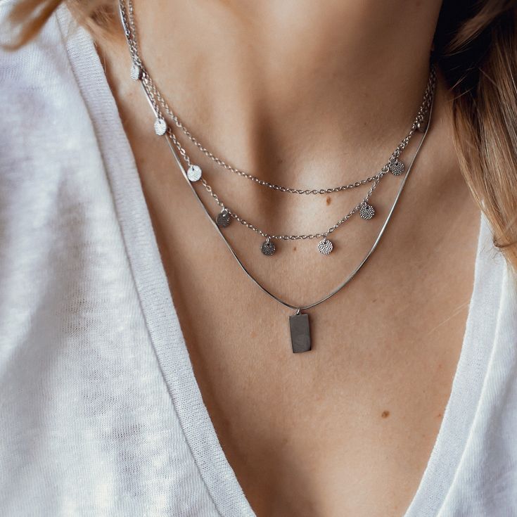 This layered necklace, made from stainless steel, consists of two different lengths of chain which connect together and close at the center back with a lobster claw clasp. The shorter chain is unadorned and sits higher on the chest than the longer chain, which has nine small circular pendants with a textured surface hanging from it. There is also a short length of chain at the back which is made from larger links and which has a small seashell charm attached to the end, making the overall fit of the necklace adjustable. Length: 41.0 cm (16.14 inches) simple chain, 42.0 cm (16.53 inches) chain with circles Length Extension: 5.5 cm (2.16 inches) Pendant Size: 0.5 cm (0.19 inches) Weight: 7.0 g (0.24 oz) Also available in rose gold and gold: Textured Circle Layered Necklace Rose Gold https:// Minimalist Double Chain Metal Charm Necklaces, Minimalist Double Chain Metal Charm Necklace, Minimalist Metal Charm Necklace With Double Chain, Silver Charm Necklaces With Chain For Layering, Silver Charm Necklaces For Layering, Silver Charm Necklace For Layering, Minimalist Metal Layered Necklace For Everyday, Everyday Metal Charm Necklaces With Double Chain, Everyday Metal Charm Necklace With Double Chain