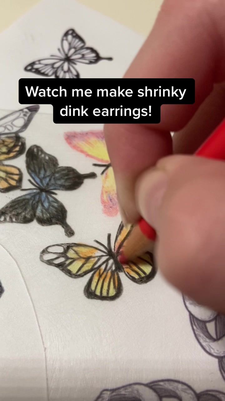 someone is drawing butterflies on the paper with a red pencil and marker, which reads watch me make shrinky pink earrings