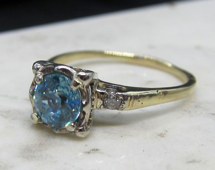 This is a gorgeous vintage estate ring that features a beautiful large Zircon.   The zircon measures 5.87mm, estimated at .90 carats.  It is held in a pretty scalloped top.   There is one diamond on each side.    They are approximately .07 carats in weight.  The Zircon has bright medium bold blue color.  The diamonds are SI clarity and eye clean.    This is a classic 1940s-50s design.   This ring is 14k white gold on top and yellow gold on the bottom.   It measures 7.7mm wide.   The finger size Vintage Diamond Rings With Accent Stones, Vintage Diamond Ring With Accent Stones For Anniversary, Vintage 14k Gold Rings With Accent Stones, Vintage Blue Diamond Wedding Ring, Heirloom Solitaire Topaz Anniversary Ring, Vintage Ring With Round Cut Accent Stones, Vintage Topaz Promise Ring With Accent Stones, Vintage Topaz Ring With Accent Stones, Vintage Rings With Round Cut Accent Stones