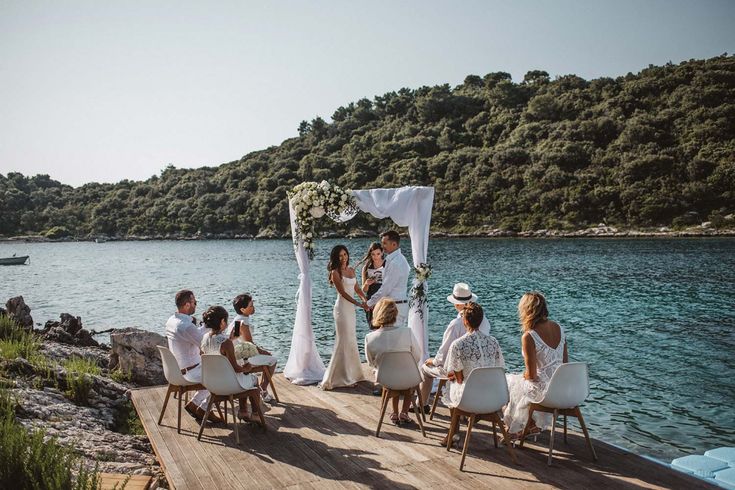 a group of people sitting on top of a wooden dock next to the ocean and trees