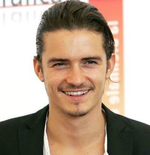 a man with a mustache smiling and wearing a black blazer over a white shirt