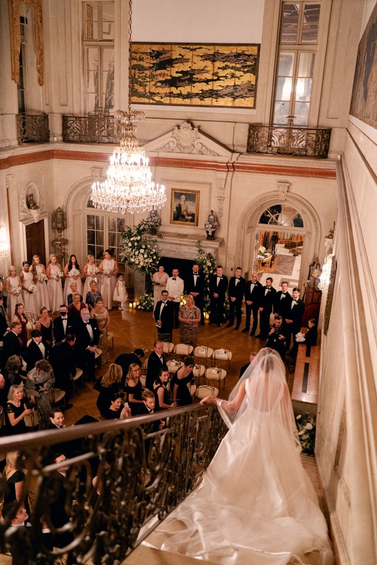 a bride and groom standing in front of their wedding party at the top of stairs