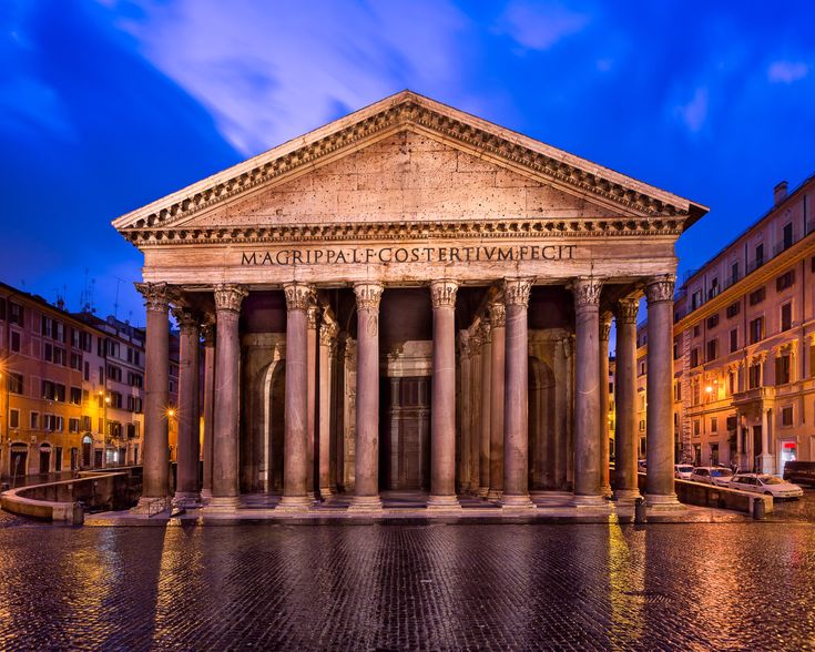 an old building with columns and pillars in the middle of a street at night time