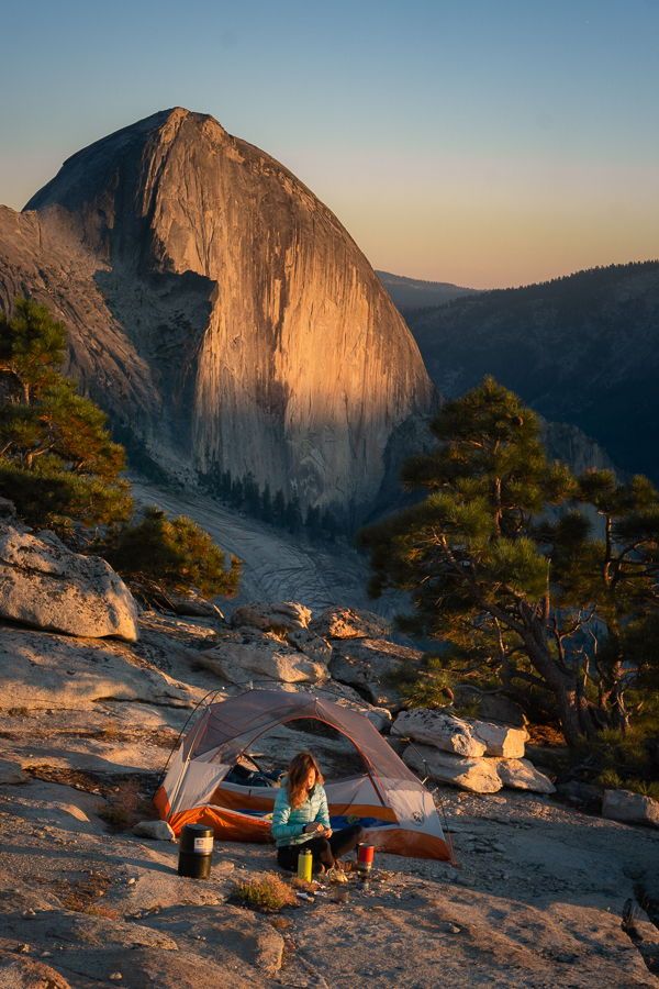 a woman sitting in front of a tent on top of a mountain next to a forest