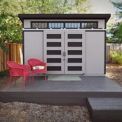 two red chairs sitting in front of a gray shed