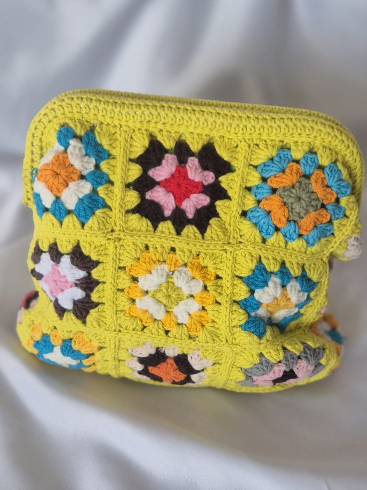 a yellow crocheted purse with multicolored flowers on it sitting on a white surface