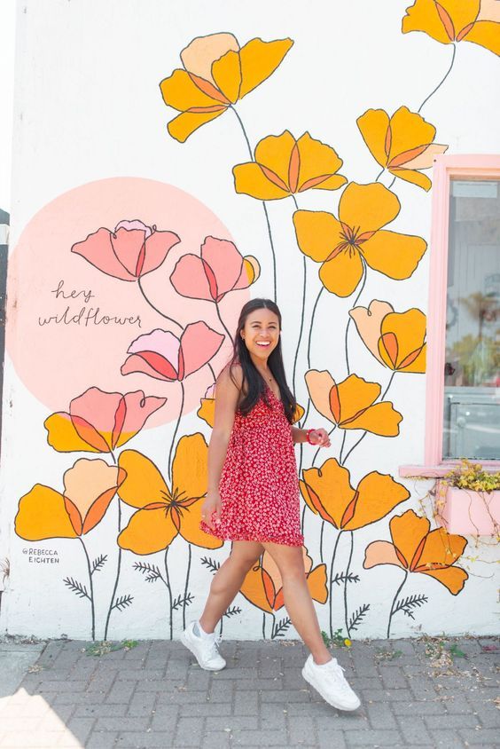 a girl standing in front of a painted wall with flowers on it and the words hello wonderful