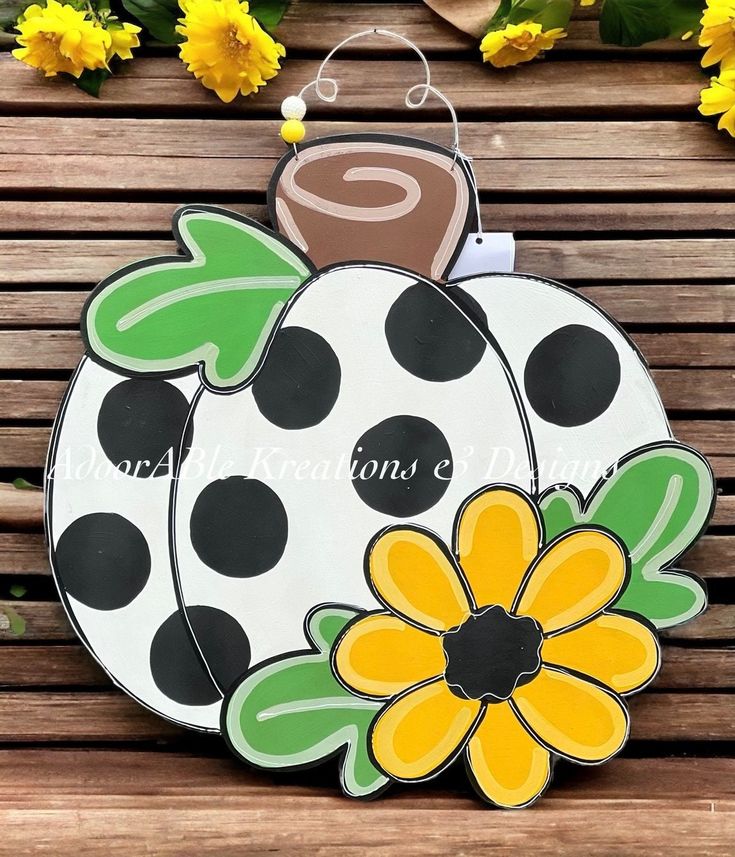 a wooden bench with a painted pumpkin and flower decoration on the front, sitting next to yellow flowers