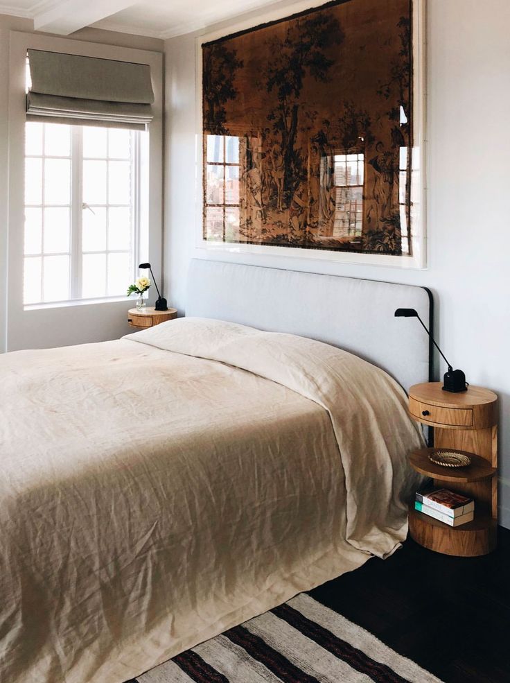 a bed sitting in a bedroom next to a window with a painting on the wall