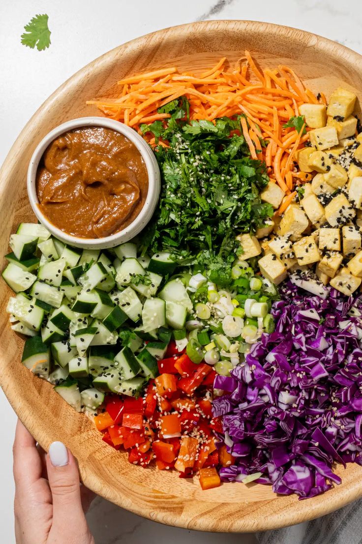 a wooden bowl filled with different types of vegetables and sauces on top of it