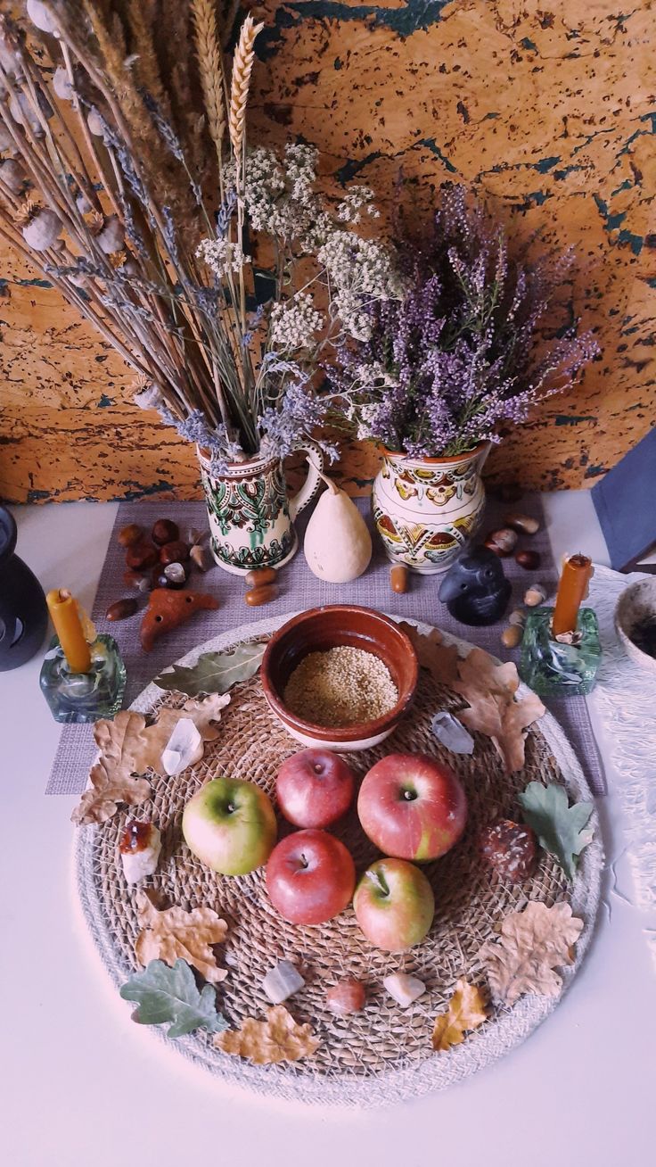 an arrangement of apples and dried flowers on a table with other items in the background