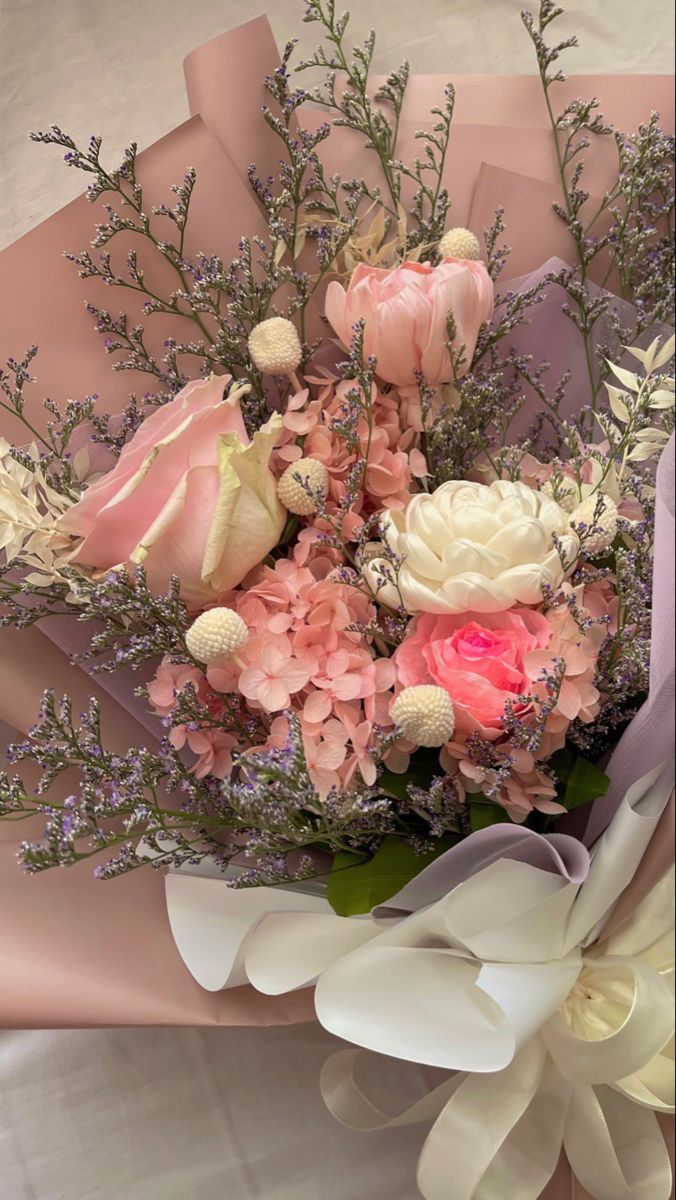 a bouquet of flowers is wrapped in pink and white paper with ribbons on the side