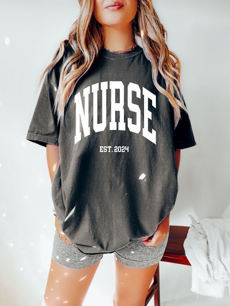 "FREE SHIPPING IN THE US! No order minimum!  Comfort Colors Nurse Shirt, Nurse Shirtk, Nurse Est 2024, Graduation Gift for Nurse, Nurse Shirt Gift, Nurse Tshirt, Gift for New Nurse ♥ The SHIRT This is a Comfort Colors 1717 shirt.  * This unisex t-shirt is intended to be loose/oversized for women to give a chic and laid back vibe. If you are looking for an oversized \"T-shirt Dress\" look, we recommend sizing up 2-3 sizes.  * Detailed sizing information can be found in the size chart in the photos.  * Printed in the USA. ♥ CARE  ＊Machine wash cold, inside-out, gentle cycle ＊Wash with mild detergent and similar colors ＊Tumble dry low or hang-dry ＊Do not bleach or fabric softeners ＊Do not iron directly onto the design ＊Do not dry clean ♥ PRODUCTION & SHIPPING ＊Each shirt is made to order. ＊Pr Oversized School Spirit T-shirt With Letter Print, School Spirit Short Sleeve T-shirt With Letter Print, Short Sleeve Tops For School Spirit Streetwear, Black Relaxed Fit Top With Name Print, Black Crew Neck Tops For School Spirit, School Spirit Relaxed Fit Top With Team Name, School Spirit Tops With Team Name In Relaxed Fit, Black Tops With Team Name Relaxed Fit, School Spirit Short Sleeve Tops With Text Print