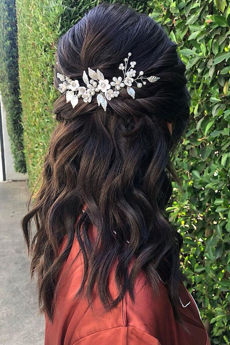 a woman wearing a hair comb with flowers on it's head in front of a hedge