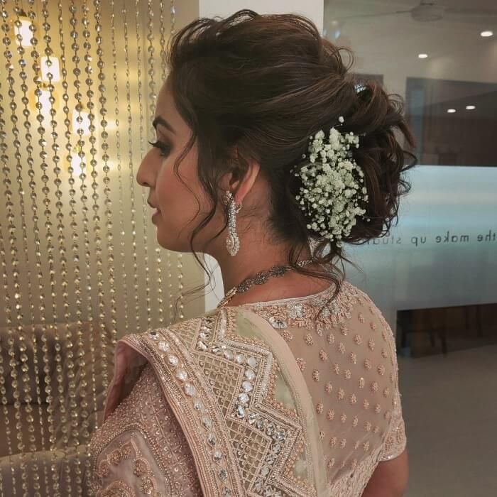 a woman in a white dress is standing near a wall with beads and pearls on it