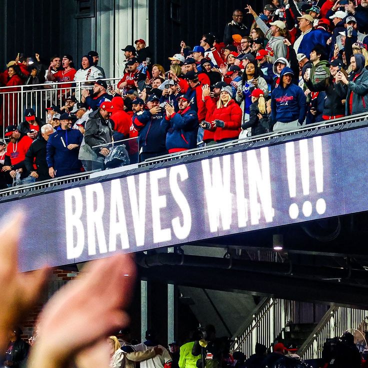 a crowd of people standing on top of a baseball field holding up signs that read braves win