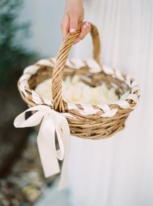 a person holding a basket with flowers in it and a white ribbon around the handle