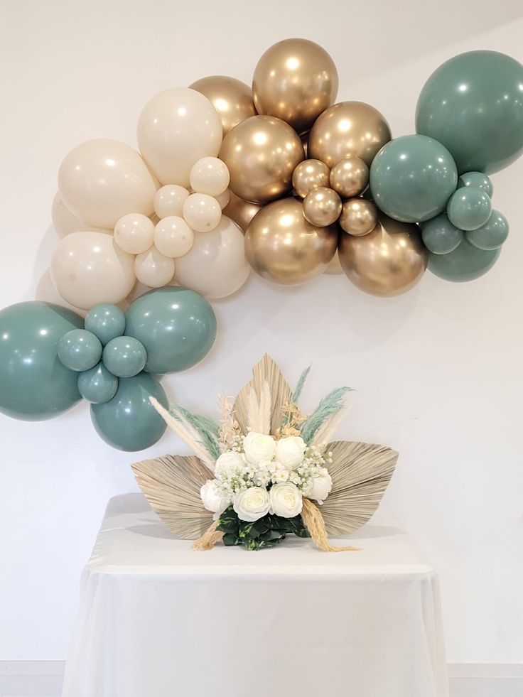 balloons and flowers on a table in front of a white wall with gold, silver and blue balloons