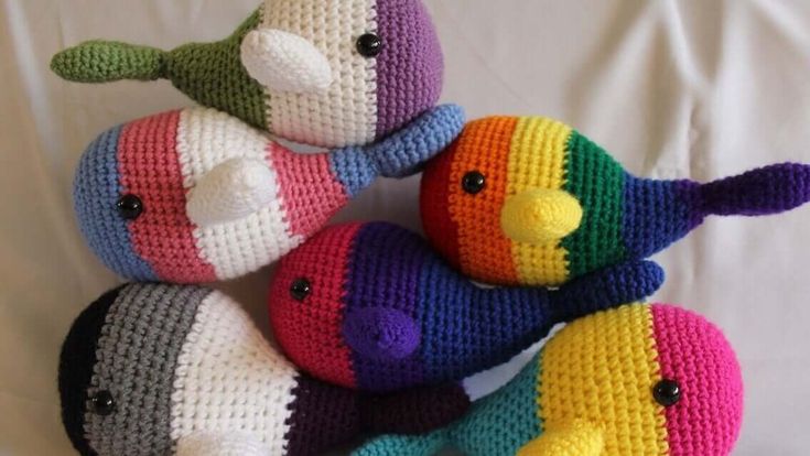 four stuffed animals are arranged in a circle on a white surface, one is multicolored and the other is crocheted