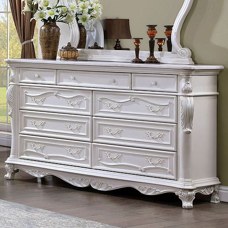 a white dresser with flowers and candles on it in front of a window, next to a mirror