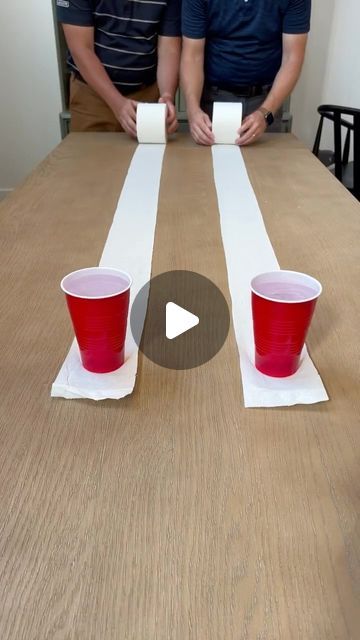 two men sitting at a table with red cups on top of it and one man standing behind them