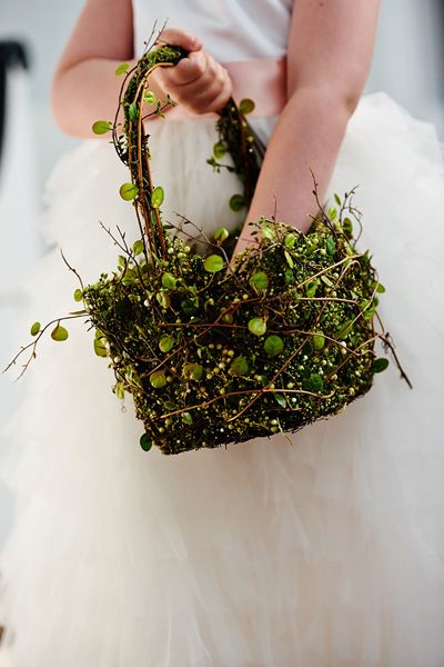 a person holding a basket with plants in it on their hand and wearing a white dress