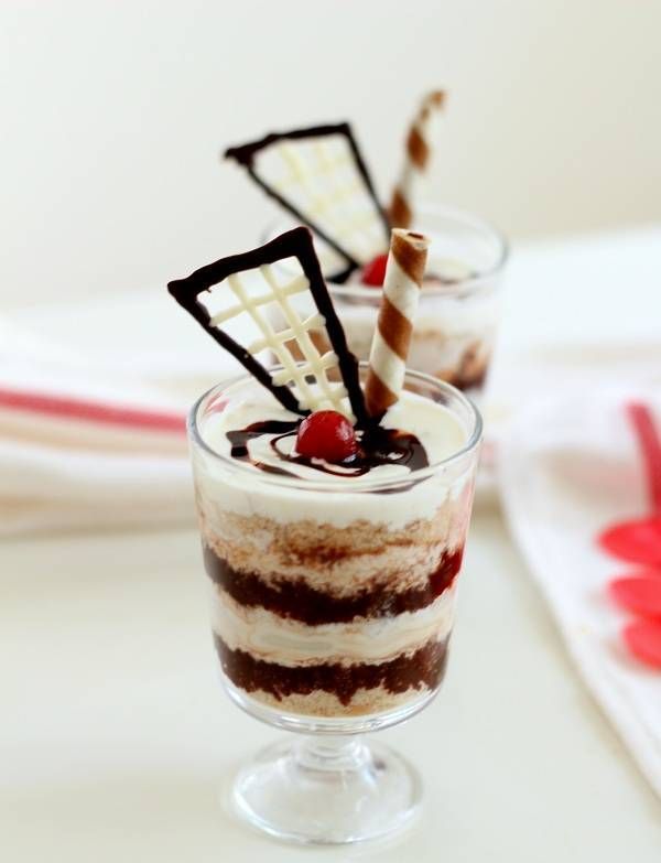 two desserts in small glasses with chocolate and cherries on the top one is red