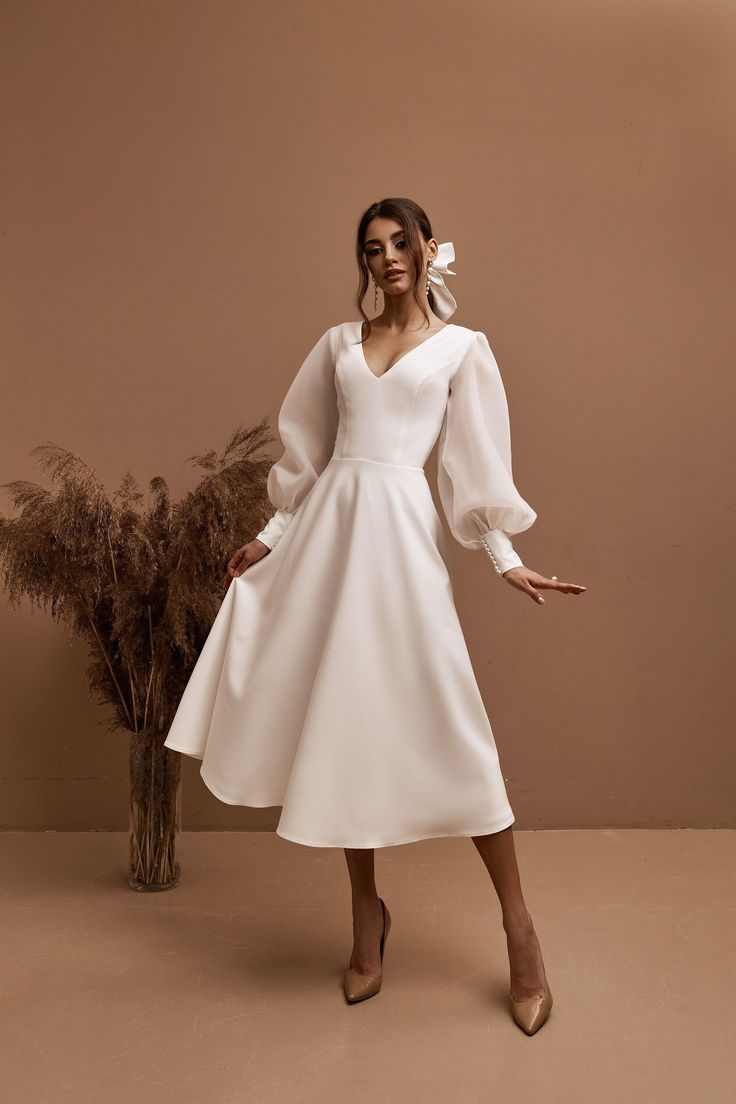 a woman in a white dress standing next to a plant