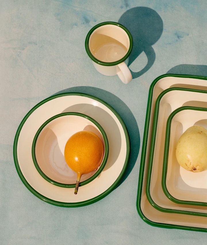 an orange sitting on top of a white plate next to two cups and saucers