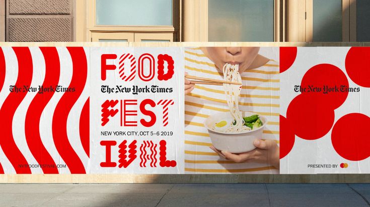 a woman holding a bowl of noodles in front of a red and white advertisement on the side of a building