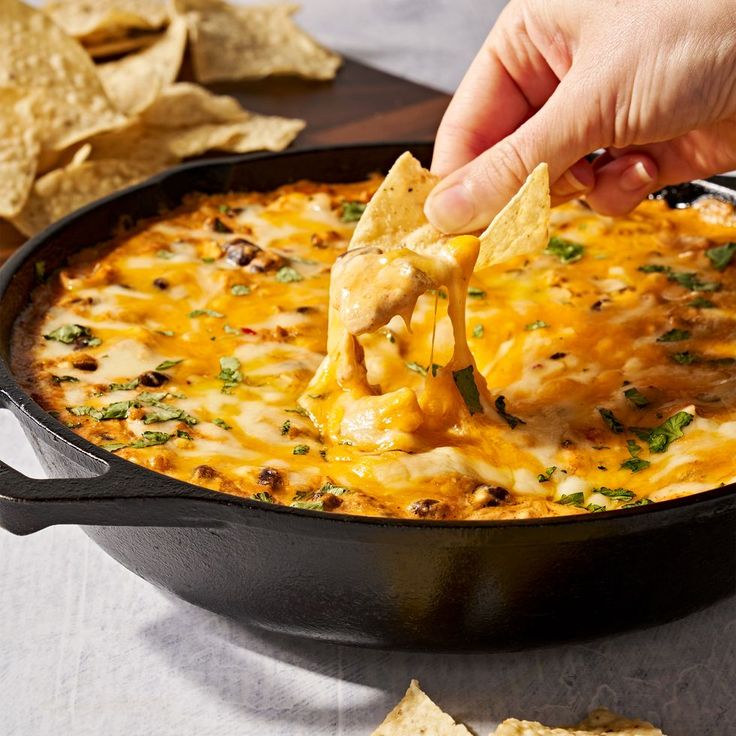 a person dipping tortilla chips into a skillet filled with cheese and sauce