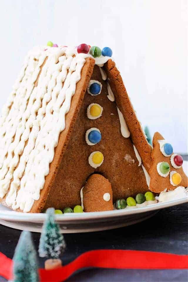 a gingerbread house with white icing and candy on the top is sitting on a plate