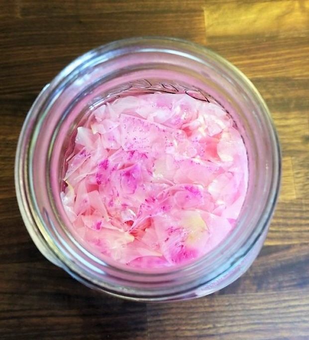 a glass jar filled with red onions on top of a wooden table