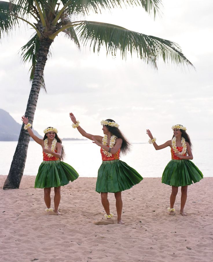 three women in green hula skirts dancing on the beach with palm trees behind them