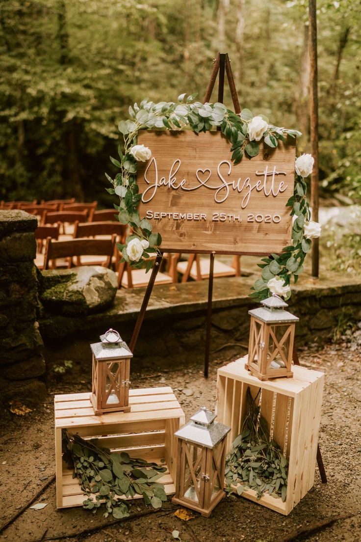 a wooden sign sitting on top of a table next to two small lanterns and greenery