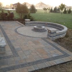 a brick patio with benches and fire pit in the back yard, surrounded by grass